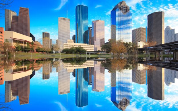 Houston Texas cityscape with tall buildings reflecting on calm water under a blue sky