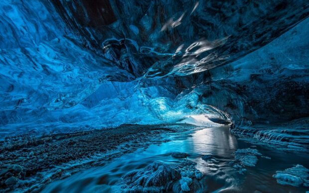 A stunning ice cave with vibrant blue ice formations and a flowing river inside the cave