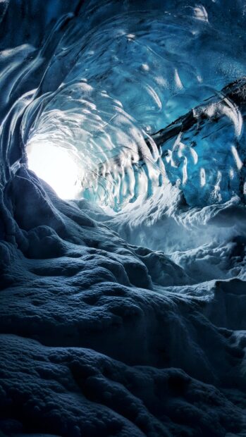Inside a blue ice cave with textured icy walls illuminated by natural light at the entrance