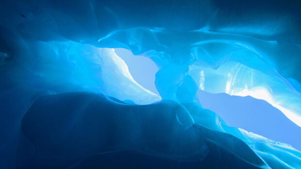 Inside view of an ice cave showing smooth blue ice formations and natural light entrance