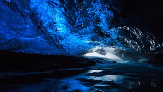 Stunning blue ice cave with reflective frozen stream and natural ice formations inside the glacier