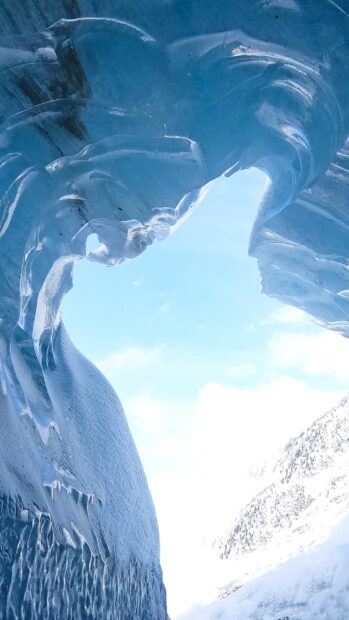 Clear ice cave formation with snowy mountain view through the opening