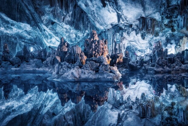 Stunning ice cave formations reflected in crystal clear water inside the cave