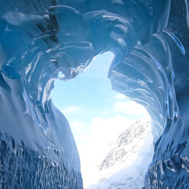 Stunning ice formation inside a blue ice cave with a view of snow covered mountains