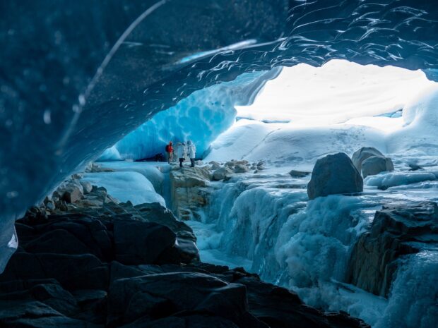 Visitors exploring blue ice cave walls and frozen landscape in a natural ice cave