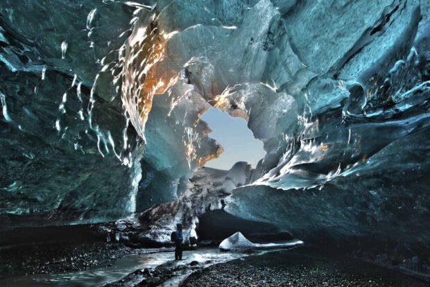 A person exploring a stunning ice cave with translucent blue ice formations and natural light opening