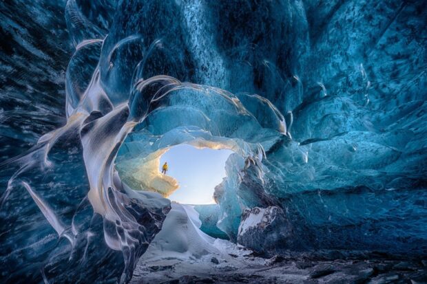 A person exploring a vast ice cave with blue ice formations inside the cave