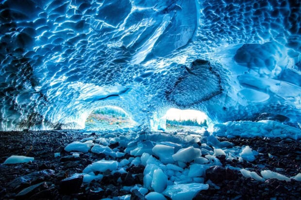 Inside the ice cave with detailed ice formations and rocky ground visible through the openings