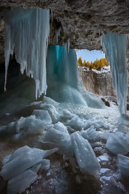 Inside a frozen ice cave with bright blue ice formations and icicles surrounding the icy floor view