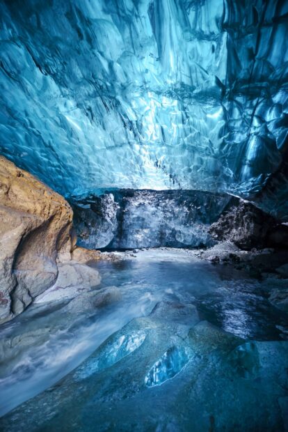 Inside a natural ice cave with flowing water and crystal clear blue ice formations