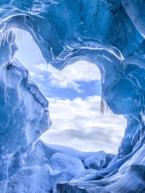 A stunning ice cave with icicles and snow formations under a cloudy sky