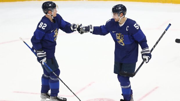 Two ice hockey players fist bump during a game in blue uniforms
