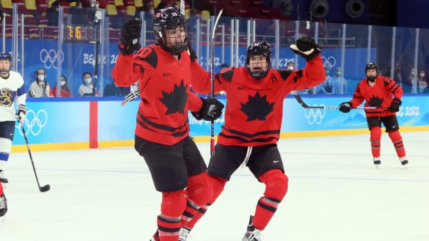 Two ice hockey players wearing red jerseys with black maple leaves celebrating on the ice rink