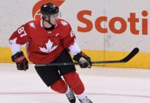 Ice hockey player wearing a red jersey with a maple leaf skating on ice rink