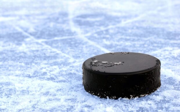Black ice hockey puck resting on snowy ice surface with skate marks