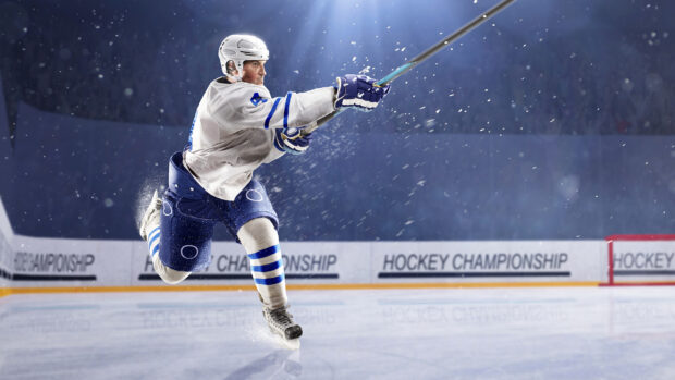 A hockey player in white and blue uniform takes a powerful shot on the ice hockey rink