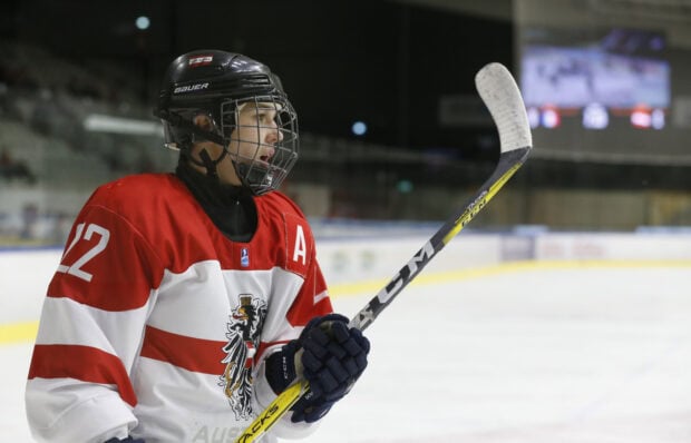 Ice hockey player wearing red and white jersey holding a hockey stick on ice rink