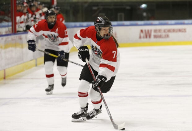 Female ice hockey player in red and white uniform skating on ice hockey rink