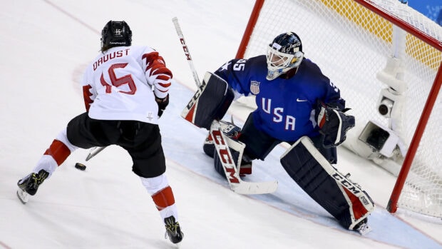 Ice hockey player in white jersey preparing to shoot the puck against the goalie in blue jersey