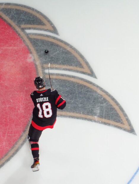Ice hockey player wearing number 18 skating on the ice near the center logo