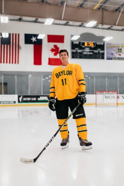 Male ice hockey player in yellow jersey standing on ice rink with hockey stick