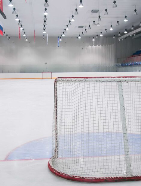 An empty ice hockey rink with a goal net in focus and bright lights above