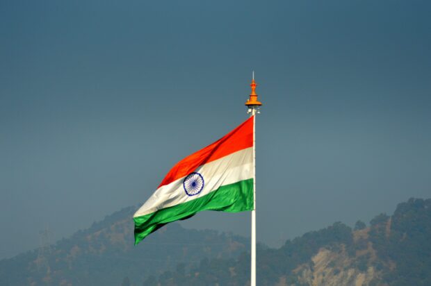 Indian flag waving on a pole with mountains in the background