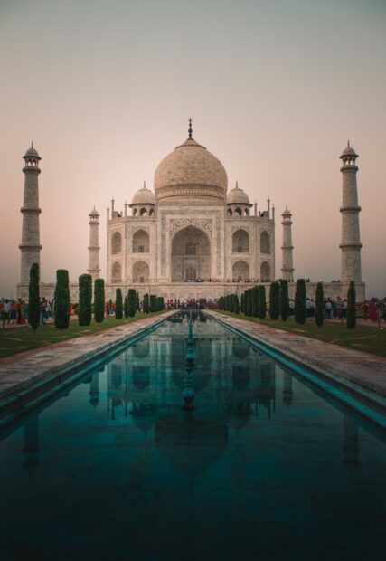 The Taj Mahal reflecting in the long pool with tourists around during sunset in India