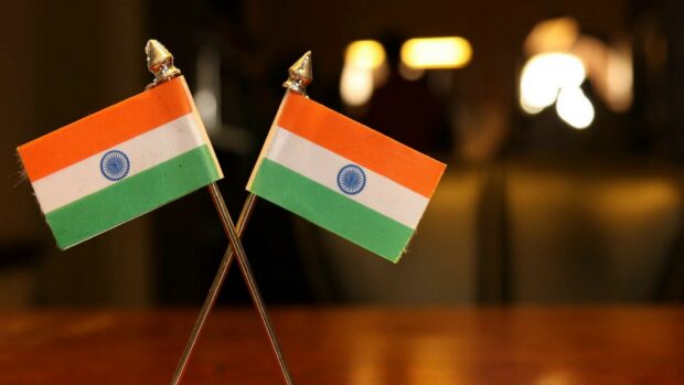 Two crossed India flags on metal poles with blurred warm background