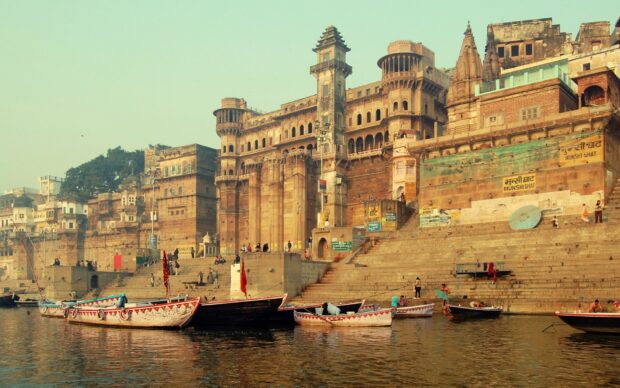 Ancient Indian architecture on riverbank with boats and people at the ghat