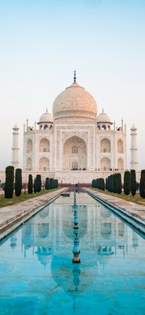 The Taj Mahal reflecting in the water with trees and blue sky in India