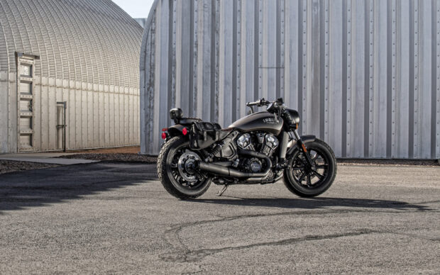 A black Indian bike parked on an asphalt surface in front of a metal industrial building