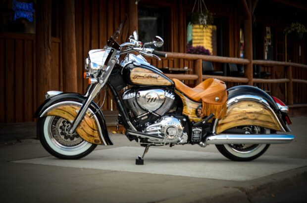A classic Indian bike with wood paneled detailing parked outside a rustic wooden building