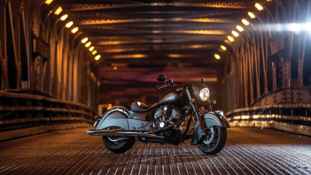 A black Indian bike parked on a metal bridge with warm yellow lights overhead