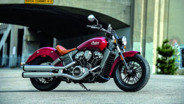 A red Indian Scout bike parked under an urban bridge with concrete surroundings
