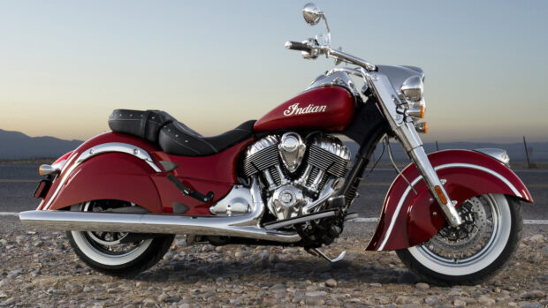 A red Indian bike parked on a rocky road with mountains in the background at sunset