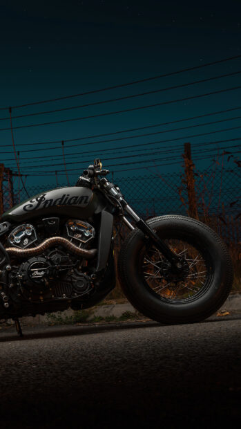 A close up of an Indian motorcycle parked on the road at night with a dark sky background