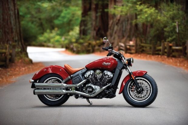Red Indian Scout bike parked on forest road with autumn leaves and tall trees in background
