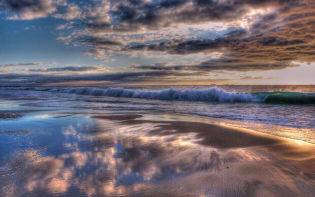 Clouds and waves reflecting on the wet sand at the Indian Ocean shore with a dramatic sky