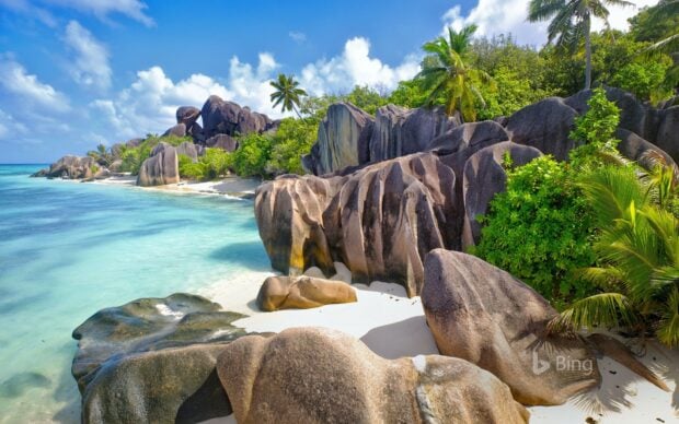 Large granite rock formations along the Indian Ocean coastline with tropical greenery