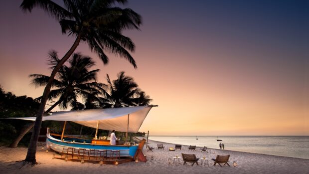 A tropical Indian Ocean scene with palm trees and a beach bar at sunset