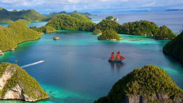 Traditional Indonesian sailing boat sailing near lush green islands in Indonesia sea