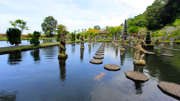 Traditional Indonesian statues along a pond with stepping stones and lush greenery in the background