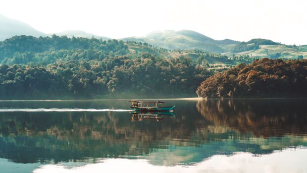 A traditional boat sailing on a calm lake surrounded by lush green hills in Indonesia