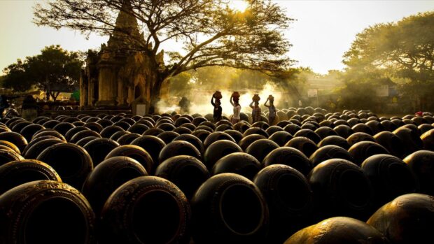 Traditional Indonesia pottery drying in the sun with workers carrying clay pots on their heads