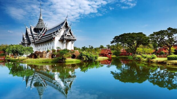 Traditional Indonesian architecture reflected in a peaceful lake with blue sky and green trees