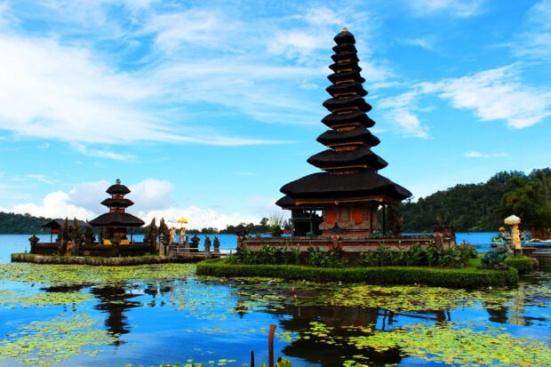 Traditional Indonesian temple on a lake surrounded by lily pads and blue sky