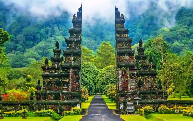 Ancient Indonesian gate surrounded by lush greenery and misty mountains in the background