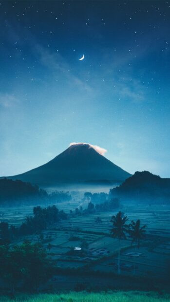 Misty mountain landscape with crescent moon over Indonesia volcano at night