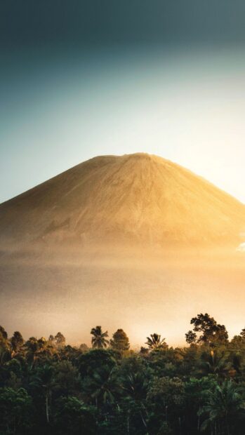 Volcanic mountain in Indonesia rising above lush tropical forest in golden sunlight